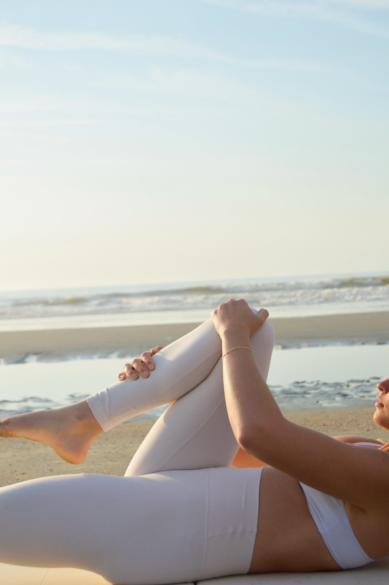 Halle in a reclined Pilates pose at the beach, lit by warm morning sun